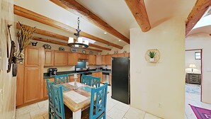 Une cuisine avec des meubles de rangement en bois, un réfrigérateur noir et une table à manger entourée de chaises bleues.