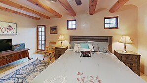 Une chambre avec un grand lit, des poutres en bois, deux fenêtres, une télévision et un bureau avec une lampe.