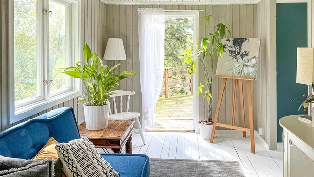 Ein gemütliches Zimmer mit einem blauen Sofa, einer weißen Lampe und einem Gemälde auf einem Lehrstuhl.