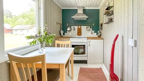 Eine kleine Küche mit einem weißen Herd, einem Holztisch und Stühlen. Ein roter Staubsauger ist rechts zu sehen.