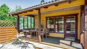 Un patio techado con terraza de madera, una mesa con sillas y un ventanal con vistas a un jardín.