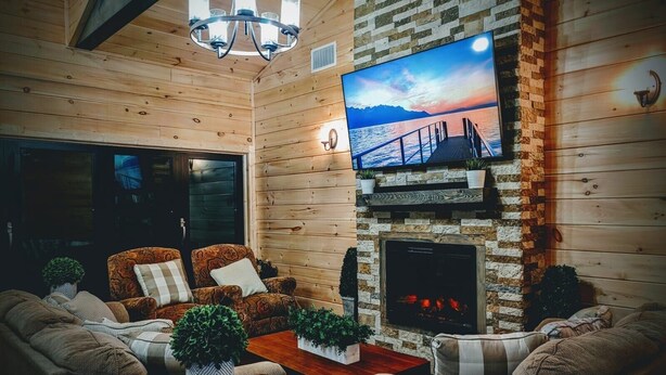 Een gezellige woonkamer met houten wanden, een open haard, een aan de muur bevestigde televisie en comfortabele zitplaatsen.