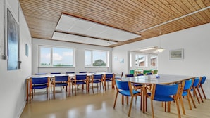 Un salón de conferencias con una larga mesa y sillas azules, ventanas amplias y techo de madera.