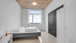 Un dormitorio moderno con cama, paredes blancas, un ventanal grande y un armario.