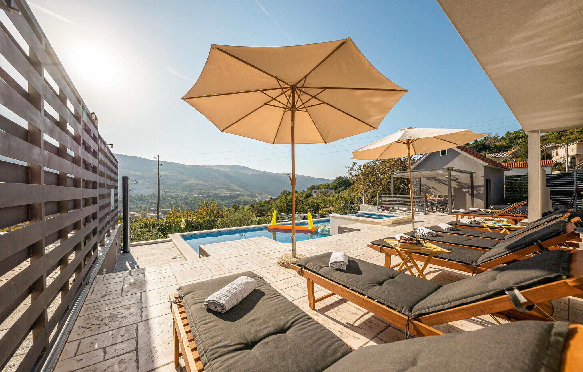 A rooftop pool area with lounge chairs, umbrellas, and a view of the mountains.