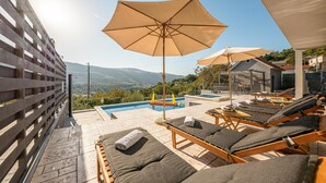 A rooftop pool area with lounge chairs, umbrellas, and a view of the mountains. - Gorgeous home in Srinjine (Srinjine)