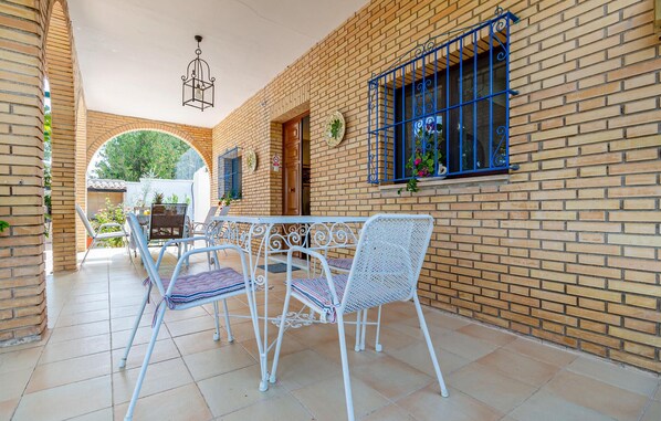 Ein überdachter Patio-Bereich mit Ziegelwand, Tisch mit Stühlen und einer hängenden Leuchte.