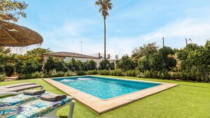 A rectangular swimming pool with a tiled edge, surrounded by well-maintained grass and various shrubs. There are two lounge chairs with towels, and a tall palm tree is visible in the background. - Lovely home in Casariche (Casariche)