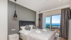 A modern bedroom with a large bed, a nightstand, a dresser, and a view of the sea through a large window. - Lovely home in Makarska (Makarska)