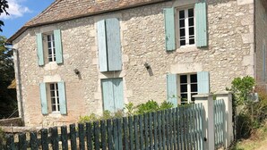 Un bâtiment en pierre avec un toit en tuiles, de nombreuses fenêtres dotées de volets et une clôture en bois.