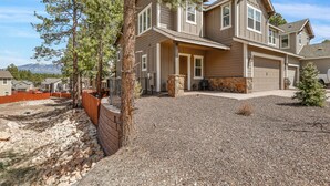 A two-story house with a stone fireplace, a covered patio, and a view of a mountain range. - Mountain Family Getaway w/AC -Sleeps 8! (Flagstaff)
