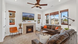 A living room with a fireplace, a ceiling fan, and large windows. - Mountain Family Getaway w/AC -Sleeps 8! (Flagstaff)