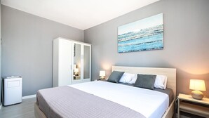 Una habitación de hotel con una cama grande, un armario, una mesita de noche con una lámpara y un cuadro colgado en la pared.