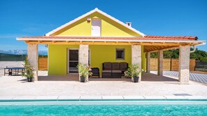 Una casa amarilla con un porche cubierto y una piscina.