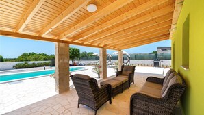 Un patio techado con mobiliario de mimbre, una piscina y vistas del paisaje.