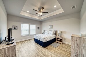 Une chambre avec un ventilateur de plafond, un lit recouvert d’une couvre-lit à motifs floraux, deux tables de chevet avec des lampes et une commode en bois.