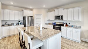 Una cocina moderna con armarios blancos, encimeras de granito, electrodomésticos de acero inoxidable y una isla central con taburetes de bar.