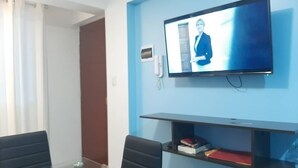 A modern room with a flat-screen TV mounted on the wall, two black chairs, a small shelf with books, and a door leading to another room. - Super cozy apartment / apartment close to the airport (Callao)