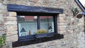 A stone building with a window featuring a black frame and a small planter with grass. - Studio Terre & Mer à Dragey (Dragey)