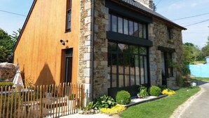 A modern house with a wooden facade and stone exterior, featuring large windows and a well-maintained garden. - Studio Terre & Mer à Dragey (Dragey)