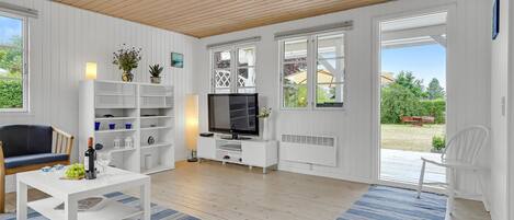 Una sala de estar moderna con interior blanco, techo de madera y ventanas amplias.