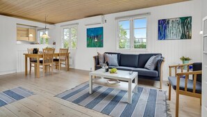 A spacious living area with a dining table, a sofa, and a coffee table. There are large windows providing natural light and views of greenery outside. - 2 bedroom amazing home in Skibby (Skibby)