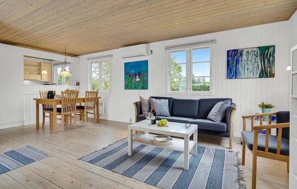 A spacious living area with a dining table, a sofa, and a coffee table. There are large windows providing natural light and views of greenery outside. - Awesome home in Skibby with WiFi (Skibby)