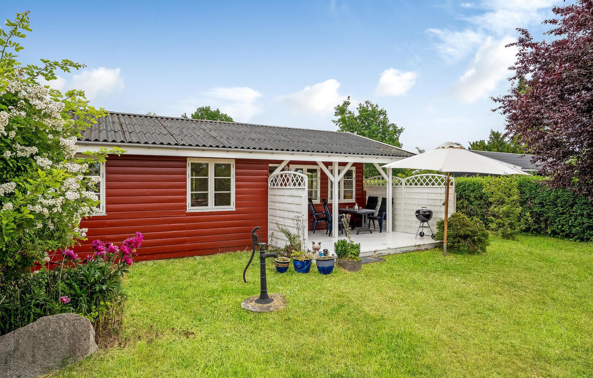 A red wooden house with a covered porch, a barbecue grill, and potted plants.