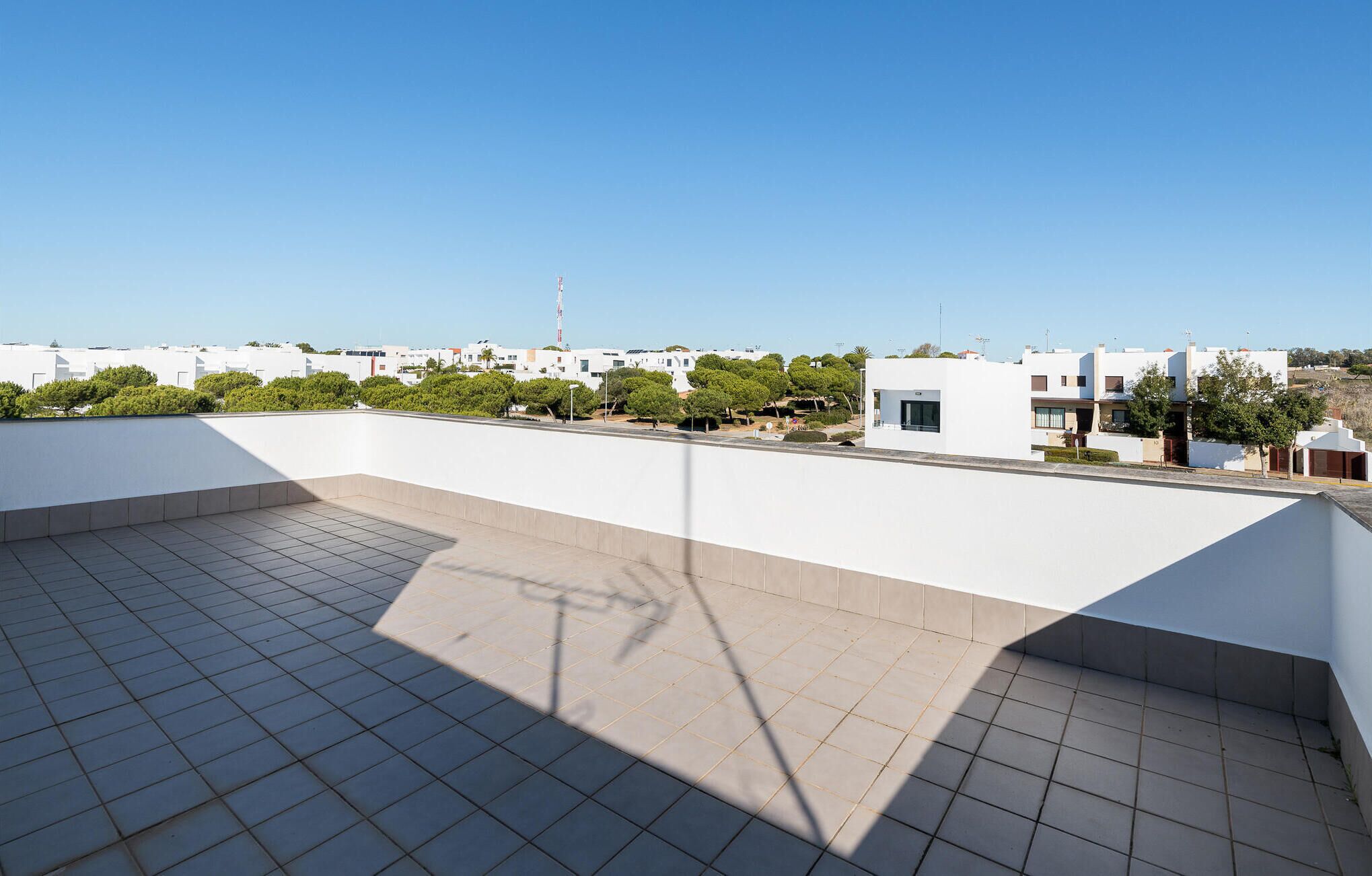Una terraza en la azotea con suelo de baldosas, cielo despejado y edificios residenciales al fondo.