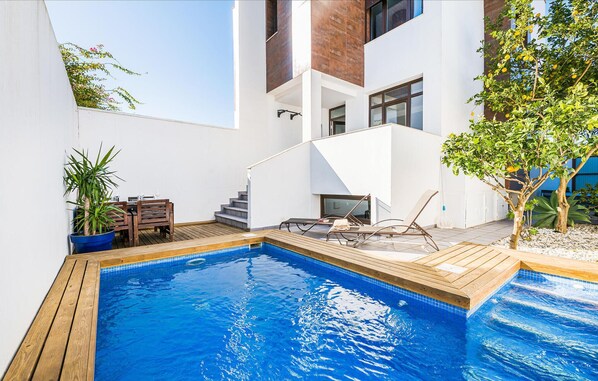 A modern outdoor swimming pool with wooden deck, lounge chairs, and a dining area with a table and chairs. - Stunning home in Conil de la frontera (Conil de la frontera)