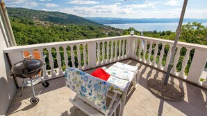 Ein Balkon mit Grill, zwei Stühlen und einem roten Sonnenschirm.