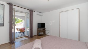 Ein Schlafzimmer mit einem großen Bett, einem Fernseher auf einem Holzständer und einer Glastür, die zu einem Außenbereich führt.