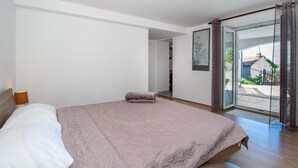 Ein Schlafzimmer mit Bett, Nachttisch, Fenster mit Blick ins Freie und einer Tür zu einem anderen Raum.