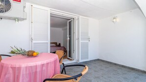 Ein Zimmer mit einem runden Tisch, der mit einer pinkfarbenen Tischdecke bedeckt ist, zwei Korbstühle, einem Ventilator und einer Tür zu einem weiteren Raum.