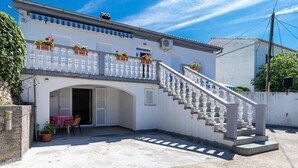 Ein weißes Gebäude mit Balkon, Treppe und einem Tisch mit Stühlen außen.