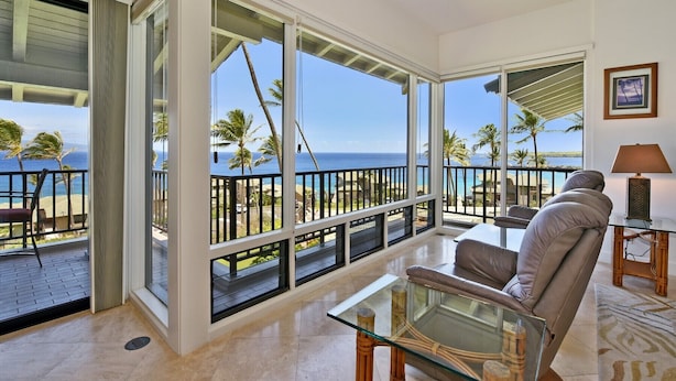 Ein geräumiger Balkon mit großen Glaswänden und Blick auf das Meer und Palmen.