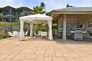 An outdoor patio with a covered seating area, a grill, and a poolside view.