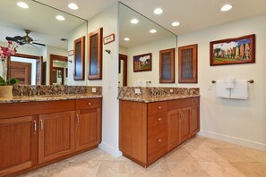 A bathroom with a double vanity, granite countertops, wooden cabinets, a large mirror, and a painting on the wall.