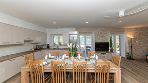 A modern kitchen with white cabinets, a dining area with wooden chairs and a glass table, and a stone wall with a TV and plant. - Awesome home in Vinisce (Vinisce)