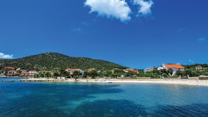 A coastal scene with clear blue waters, a small boat, and a hill with houses in the background. - Awesome home in Vinisce (Vinisce)
