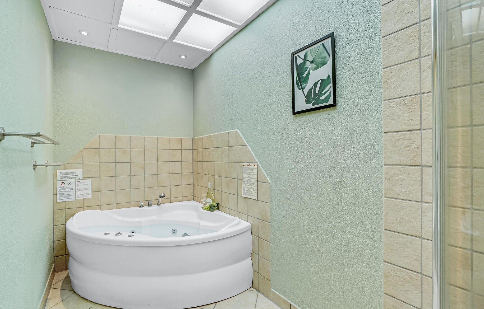 A bathroom with a freestanding bathtub, a glass shower enclosure, and a framed plant on the wall.