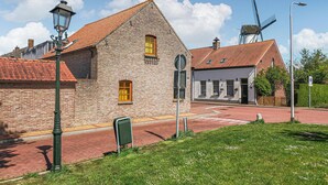Een klassiek bakstenen gebouw met een rood pannendak, een windmolen op de achtergrond en een straat met een zebrapad.