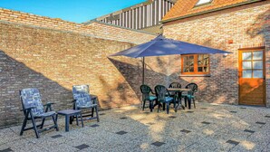 Een terras met tafel en stoelen, een grote parasol en een bakstenen muur.
