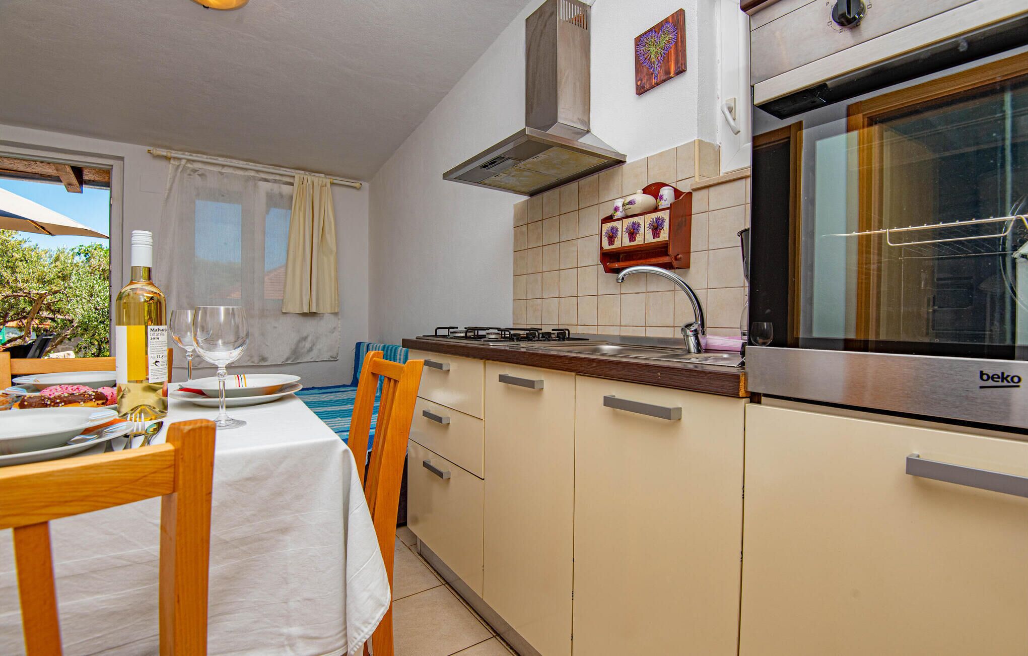 Una cucina con piano cottura a gas, lavello e forno Beko. C'è un tavolo da pranzo con sedie e una bottiglia di vino.