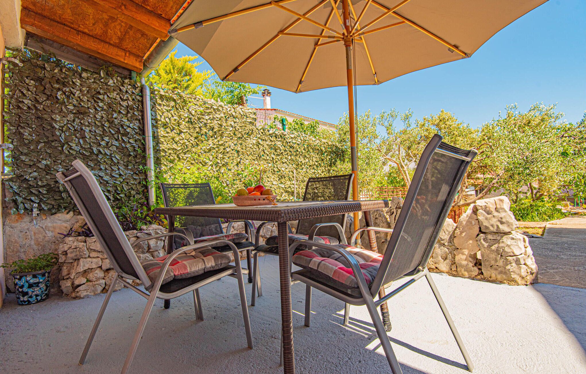 Un patio al aire libre con una mesa, sillas, un paraguas grande y un muro de piedra.