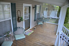 Une terrasse en bois avec une porte vitrée, deux chaises en métal, une petite table et un pot de fleurs.