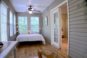 Une chambre à coucher avec un lit, un bureau et une chaise. Il y a un ventilateur de plafond et une fenêtre avec des stores.