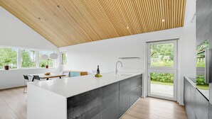 Eine moderne Küche mit einer großen Kochinsel, einer integrierten Spüle und Blick auf den Garten durch große Fenster.