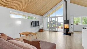 Ein geräumiges Wohnzimmer mit hoher Decke, großen Fenstern, einem Kamin und einem Fernseher.