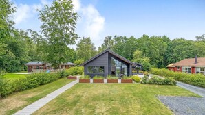 Ein modernes Haus mit einem großen Glasfenster, umgeben von einem gepflegten Garten und einem gepflasterten Weg.